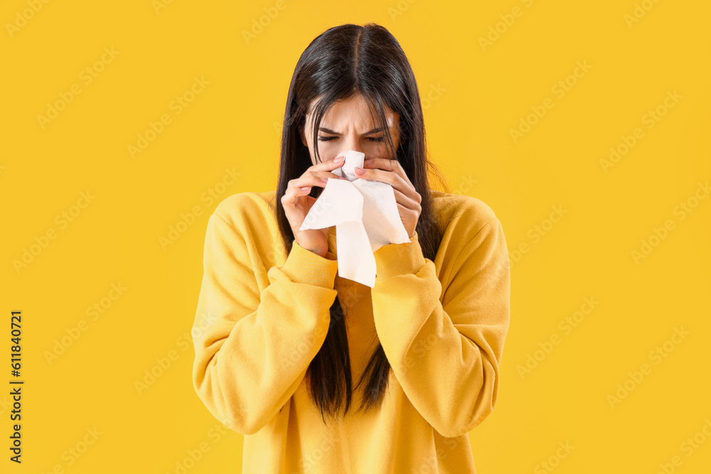 Allergic young woman with tissue sneezing on yellow background Allergic young woman with tissue sneezing on yellow background