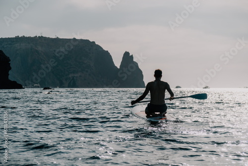 Side view foto of a man swiming and relaxing on the sup board. Sportive man in the sea on the Stand Up Paddle Board SUP. The concept of an active and healthy life in harmony with nature.