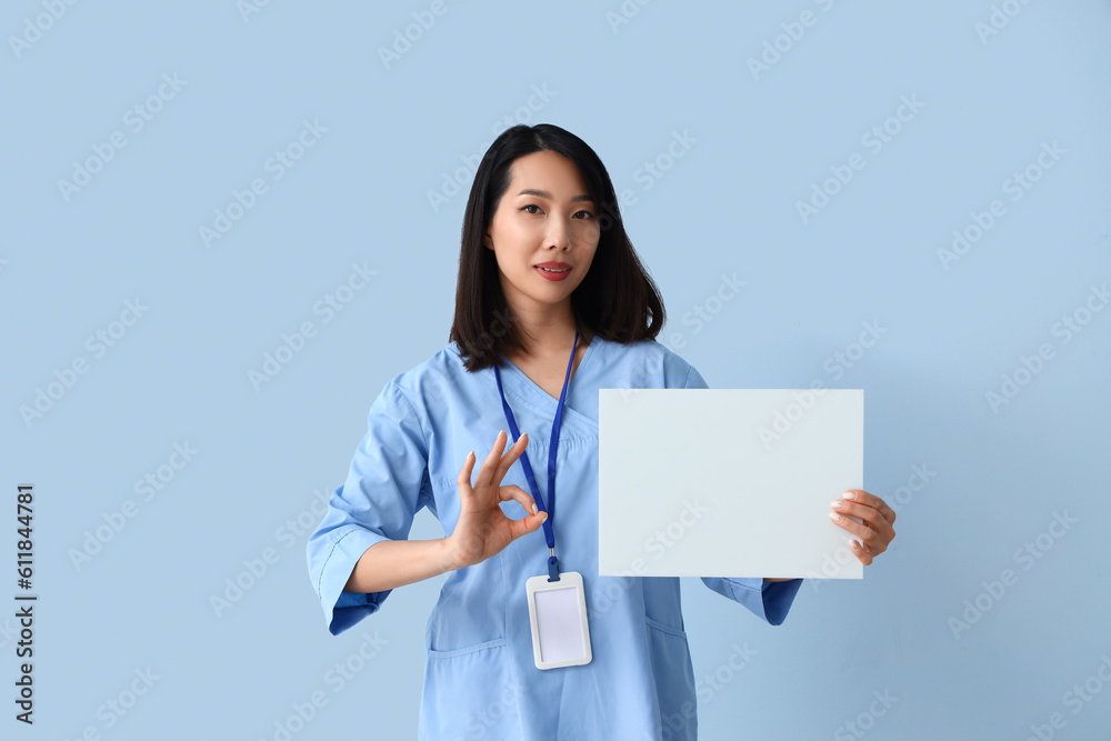 Female Asian medical intern with blank paper sheet on blue background Female Asian medical intern with blank paper sheet on blue background