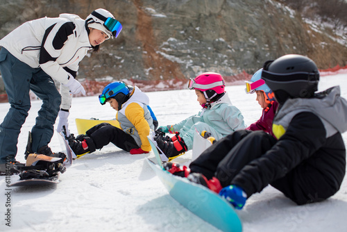 Children learning how to snowboard with their coach photo