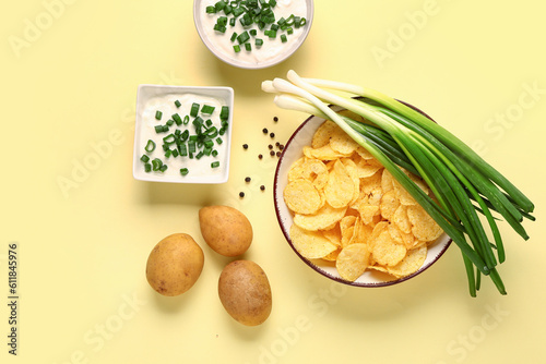 Bowls of tasty sour cream with sliced green onion and potato chips on yellow background