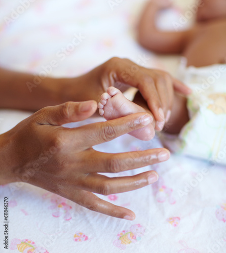 Hands, newborn and closeup of a baby foot with mother rubbing for comfort, care and love. Childcare, cute and zoom of a woman touching her premature infant child feet in her crib at their home.