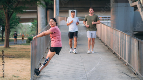Woman exercising in a park with a friend providing support while using a prosthetic leg. People jogging side by side outside in a park. Female walking and exercise works out outside.