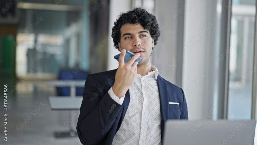Young latin man business worker using laptop sending voice message by smartphone at office Young latin man business worker using laptop sending voice message by smartphone at office