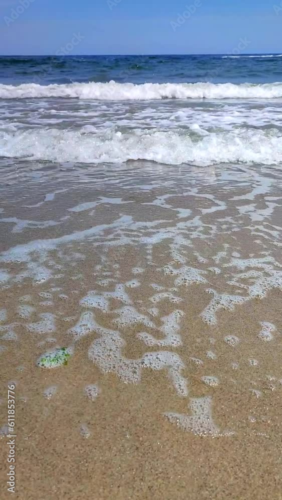 Blue sea, waves, white foam, sandy beach, shore on sunny summer day. Blue sea waves with white foam crashing over sandy seashore sunny day. Seascape waterscape scenery landscape view. Vertical