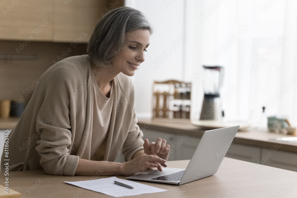 Cheerful mature freelancer woman working from home, using job application on laptop computer, enjoying internet technology for remote freelance job, online communication, smiling Cheerful mature freelancer woman working from home, using job application on laptop computer, enjoying internet technology for remote freelance job, online communication, smiling