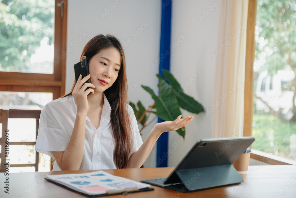 Business asian woman Talking on the phone and using a laptop with a smile while sitting at office.. Business asian woman Talking on the phone and using a laptop with a smile while sitting at office..