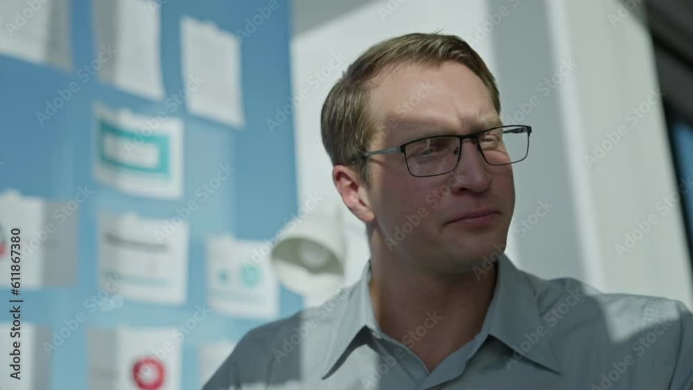 Businessman sits at computer in office by large window, picks up document and looks through pages Businessman sits at computer in office by large window, picks up document and looks through pages