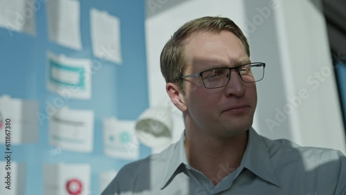 Businessman sits at computer in office by large window, picks up document and looks through pages photo