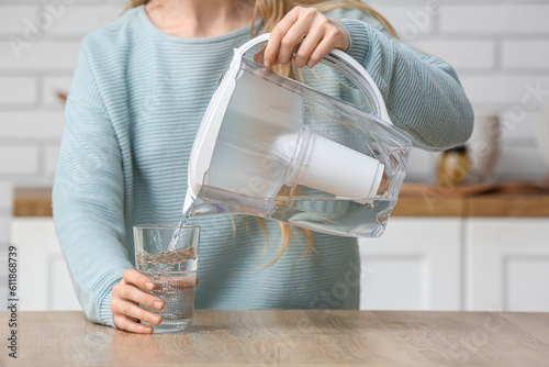 Schilderij op canvas Woman pouring water into glass from filter jug at table in kitchen