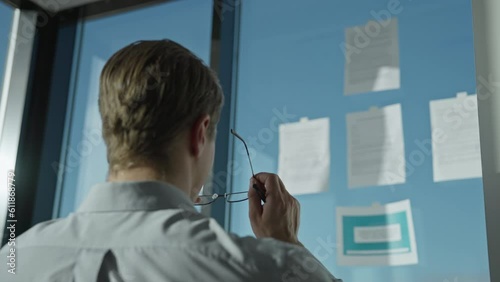 Businessman looks at hanging documents, puts on glasses, and begins to study them photo