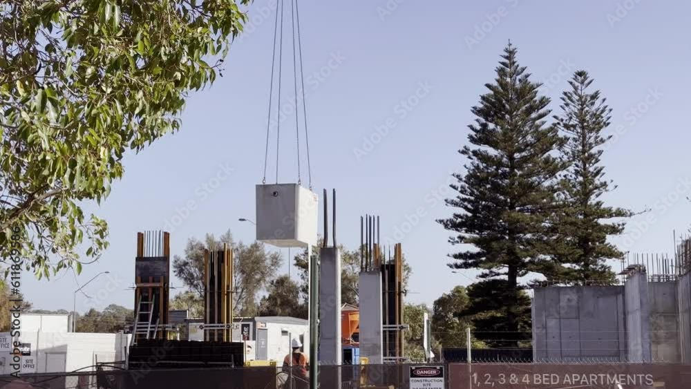 custom made wallpaper toronto digitalCrane slowly lowers large concrete block onto building site - tree branch in foreground, large pine trees in background beneath clear blue sky