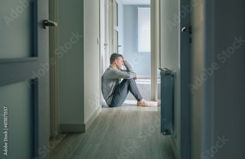 Desperate man with mental disorder and suicidal thoughts holding his head with hand sitting on the floor of a mental health center