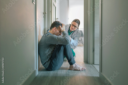 Female psychiatrist reassuring and helping with empathy to male patient sitting on the room floor of mental health center