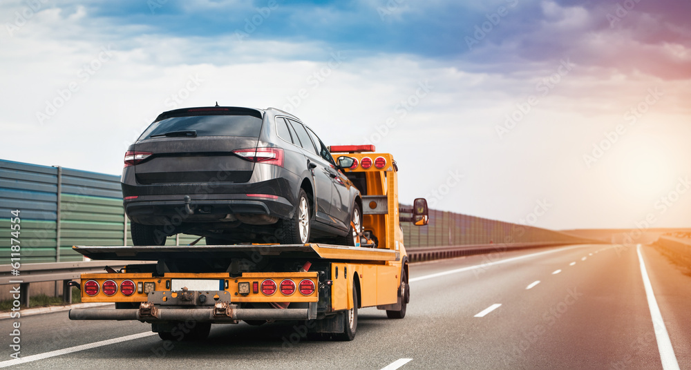 A tow truck on the public road. Tow truck with broken car on country road. Tow truck transporting car on the highway. Car service transportation concept. - obrazy, fototapety, plakaty 