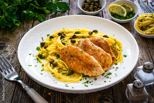Chicken piccata with spaghetti and capers in sauce on wooden background
 photo
