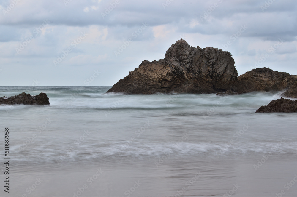 Rocks beaten by waves on the beach with cloudy sky Rocks beaten by waves on the beach with cloudy sky