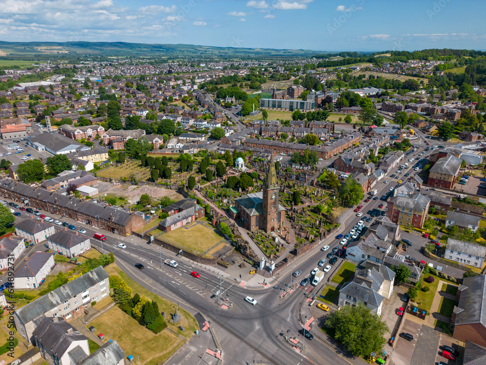 This aerial drone photo shows the town of Dumfries in the district of Dumfries and Galloway in Scotland. You can see a beautiful church with a graveyard in a residential area. 
