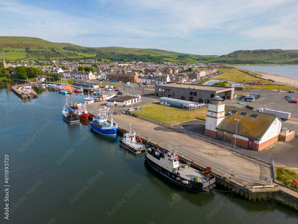 This aerial drone photo shows the harbour of Girvan at the Irish Sea in Scotland. There are many fisher boats docked in this port. Girvan is a small town and it is sunny summer weather. 
