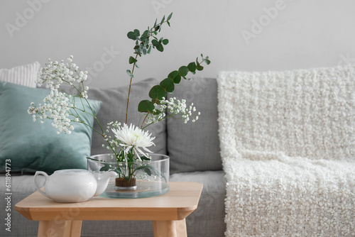 Beautiful ikebana with teapot on table in living room