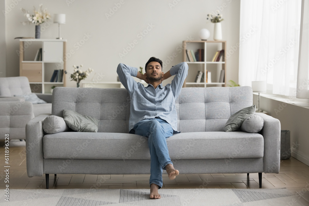 Serious calm young Indian man resting on home couch, sleeping, enjoying leisure time, silent peaceful break, pause, relaxing, sitting on comfortable sofa in modern cozy apartment Serious calm young Indian man resting on home couch, sleeping, enjoying leisure time, silent peaceful break, pause, relaxing, sitting on comfortable sofa in modern cozy apartment