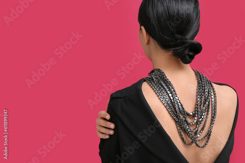 Beautiful young woman wearing massive necklace near red wall  back view