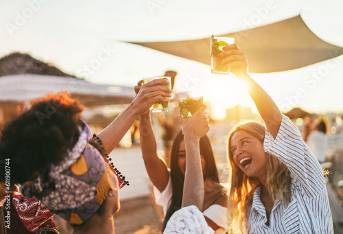 Multiracial happy friends cheering and drinking mojitos at beach party - Focus on left hand holding cocktail photo