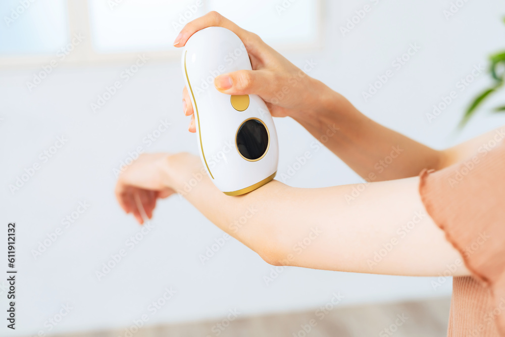 A woman using an epilator to remove unwanted arm hair at home. Stock