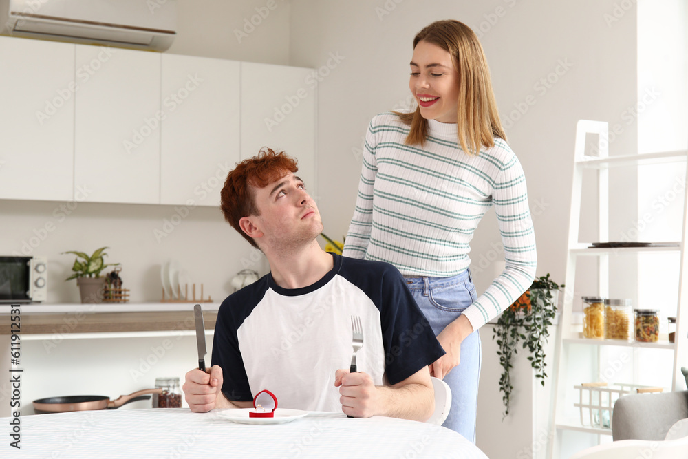 Obraz premium Young woman proposing to her upset boyfriend at table in kitchen