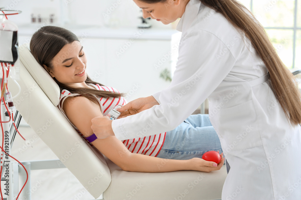 Fototapeta premium Female doctor preparing young donor for blood transfusion in clinic
