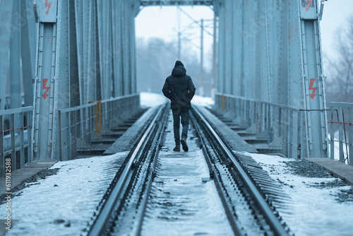 Alone man in black clothes walks along the railway track in winter. The guy walks away. Film toning