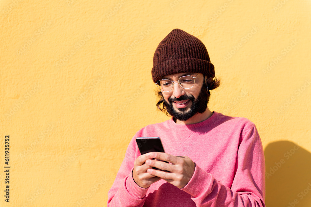 Fototapeta premium smiling young man using mobile phone in a yellow background, concept of technology of communication and modern lifestyle, copy space for text