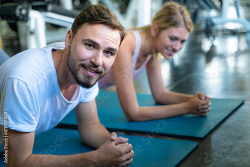 Smart man and woman buddy doing push up exercises and planking at indoor physical fitness