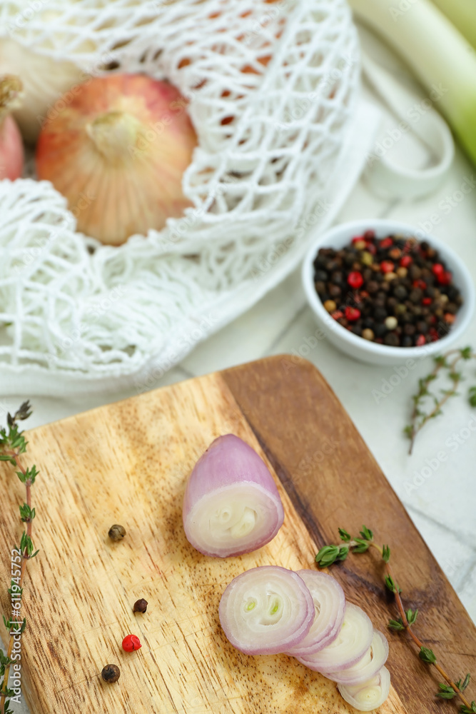 Wooden board and string bag with different kinds of onion on white tile background Wooden board and string bag with different kinds of onion on white tile background