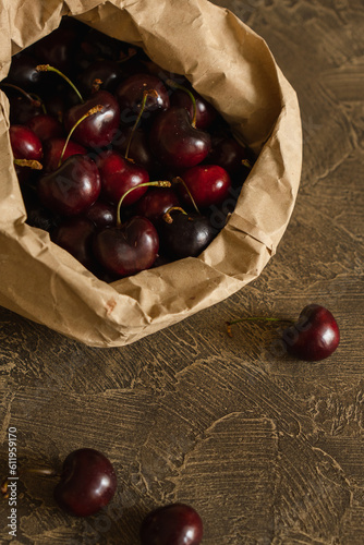 Ripe cherry berries in craft paper package on brown background