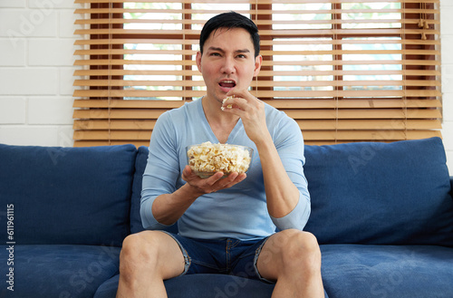 young handsome man watching movies and eating popcorn in a living room