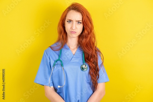 young red-haired doctor woman over yellow studio background Pointing down with fingers showing advertisement, surprised face and open mouth