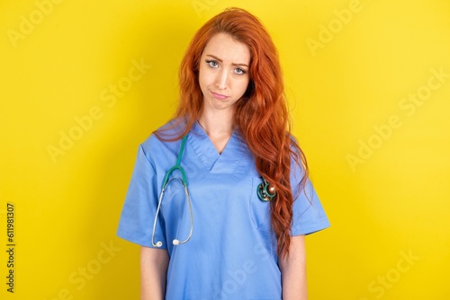 young red-haired doctor woman over yellow studio background depressed and worry for distress, crying angry and afraid. Sad expression.