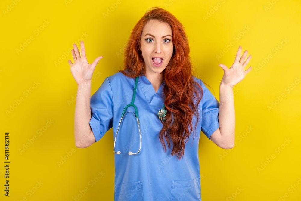 Delighted positive young red-haired doctor woman over yellow studio background opens mouth and arms palms up after having great result Delighted positive young red-haired doctor woman over yellow studio background opens mouth and arms palms up after having great result