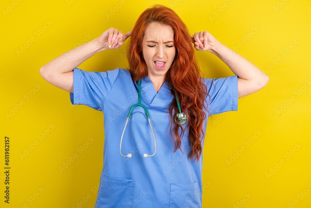 Photo of crazy young red-haired doctor woman over yellow studio background screaming and pointing with fingers at hair closed eyes Photo of crazy young red-haired doctor woman over yellow studio background screaming and pointing with fingers at hair closed eyes