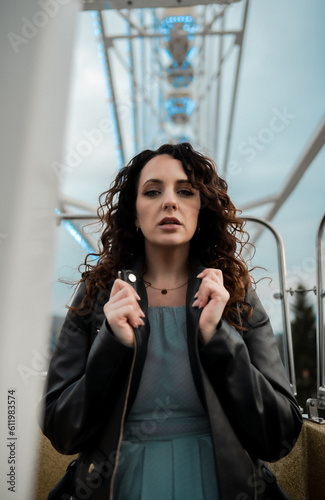 Portrait of a young beautiful confident woman with dark curly hair model posing during a giant ferris wheel ride in luna park. 