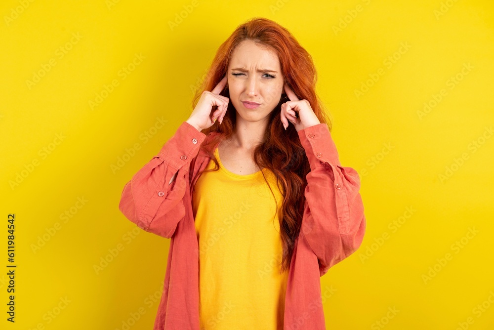 young beautiful red haired woman covering ears with fingers with annoyed expression for the noise of loud music. Deaf concept. young beautiful red haired woman covering ears with fingers with annoyed expression for the noise of loud music. Deaf concept.