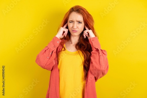 young beautiful red haired woman covering ears with fingers with annoyed expression for the noise of loud music. Deaf concept.