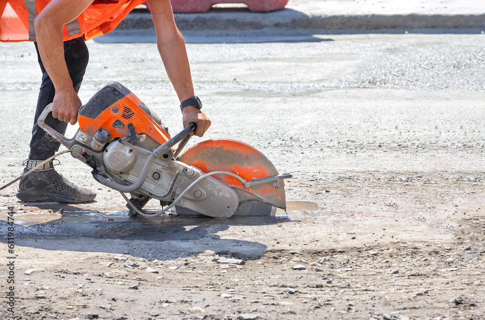 A petrol disc cutter in the hands of a worker cuts the asphalt concrete road surface on a sunny summer day.