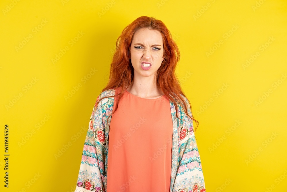 young beautiful red haired woman keeps teeth clenched, frowns face in dissatisfaction, irritated because of much duties. young beautiful red haired woman keeps teeth clenched, frowns face in dissatisfaction, irritated because of much duties.