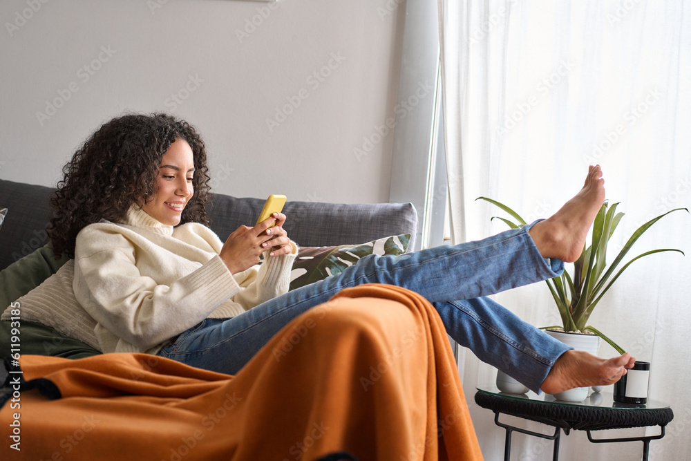 Smiling relaxed young latin woman sitting on couch using cell phone at ...