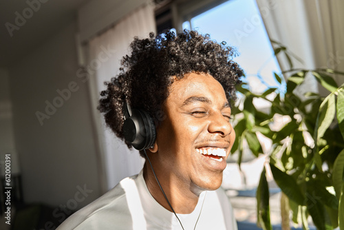 Foto Happy funky gen z hipster African American guy wearing headphones laughing at home, listening music, having fun feeling relaxed standing in living room at home