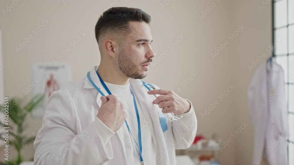 Young hispanic man doctor standing with serious expression wearing stethoscope at clinic Young hispanic man doctor standing with serious expression wearing stethoscope at clinic
