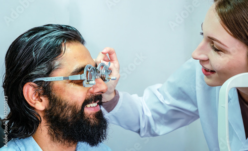 Young Caucasian woman ophthalmologist examining young man with beard with optometry for better eyesight.  Eye care concept.