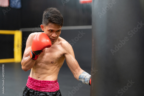 Asian boxer athlete man with red boxing glove training by punching to sandbag at the gym